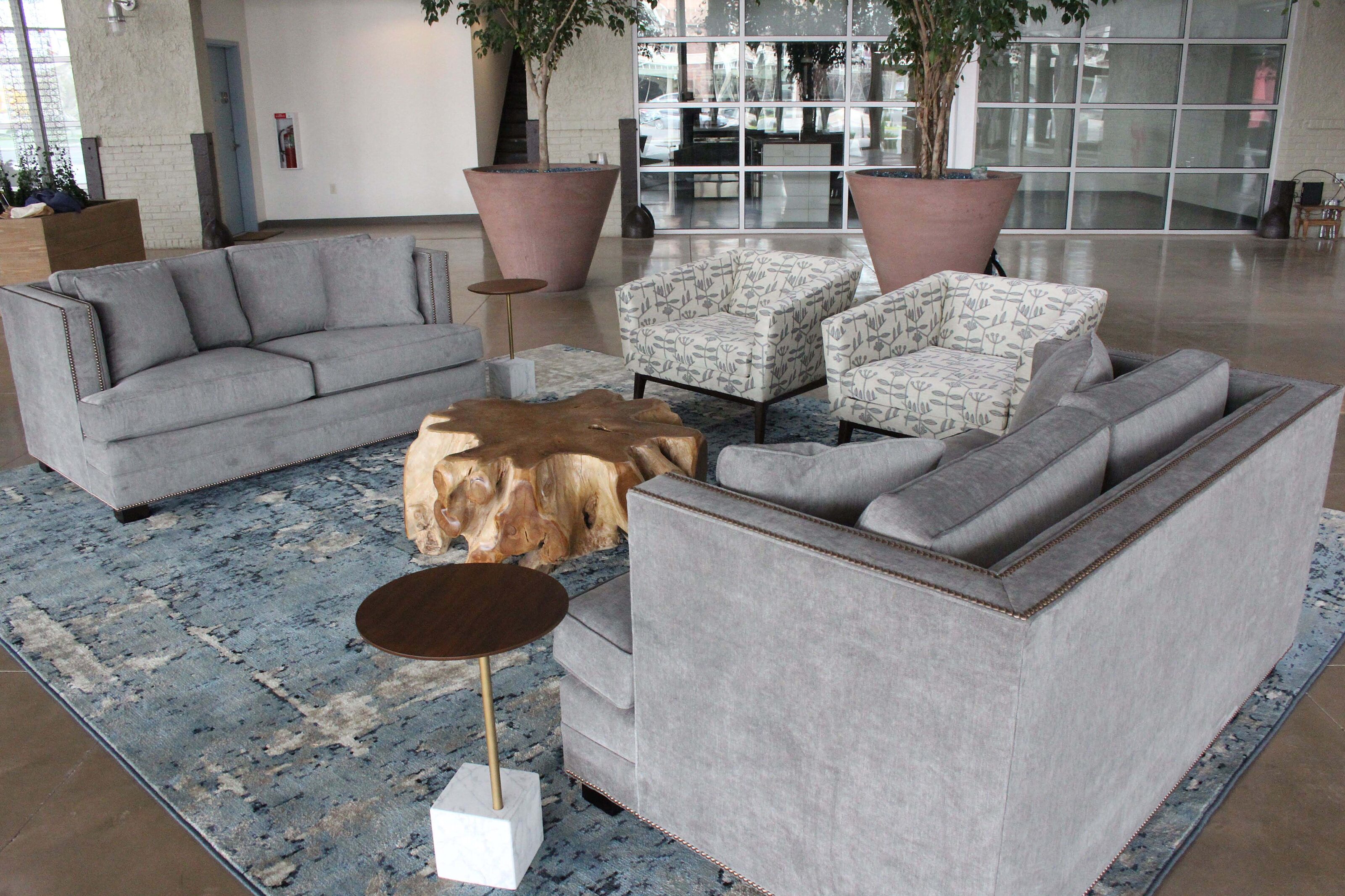 Living space with blue patterned rug. Natural wood coffee table with grey couches and white patterned chairs around in square shape
