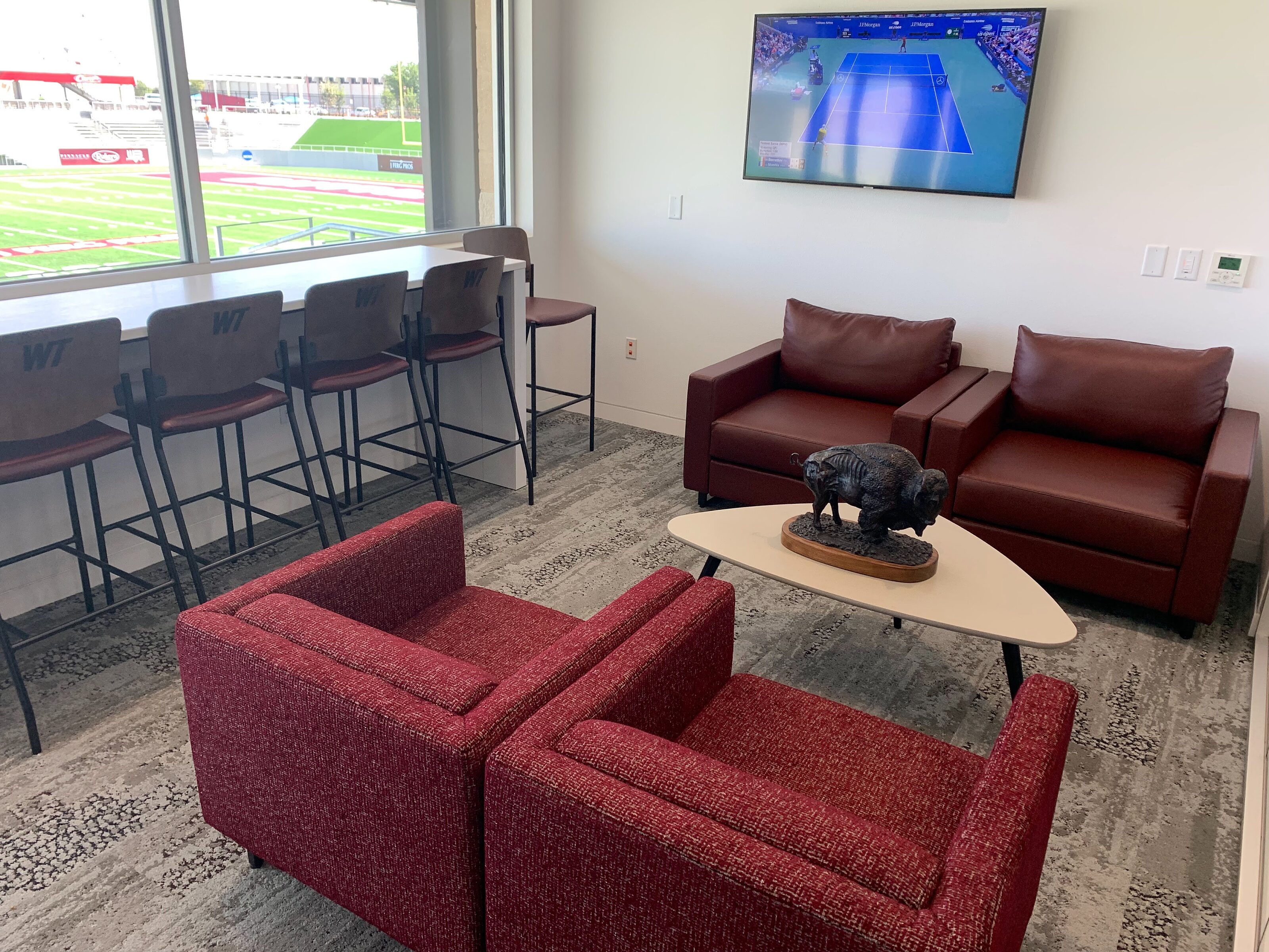 Box seating at football stadium. Tall chairs facing out windows. 2 sets of red square shaped chairs facing each other with triangle coffee table