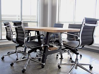 small meeting room surrounded by full length windows. modern wood and black metal table with black and chrome office chairs surround it.